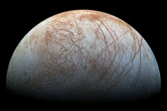 Jupiter's icy moon Europa seen from space, its cracked white and brown ice shell glowing against black space.