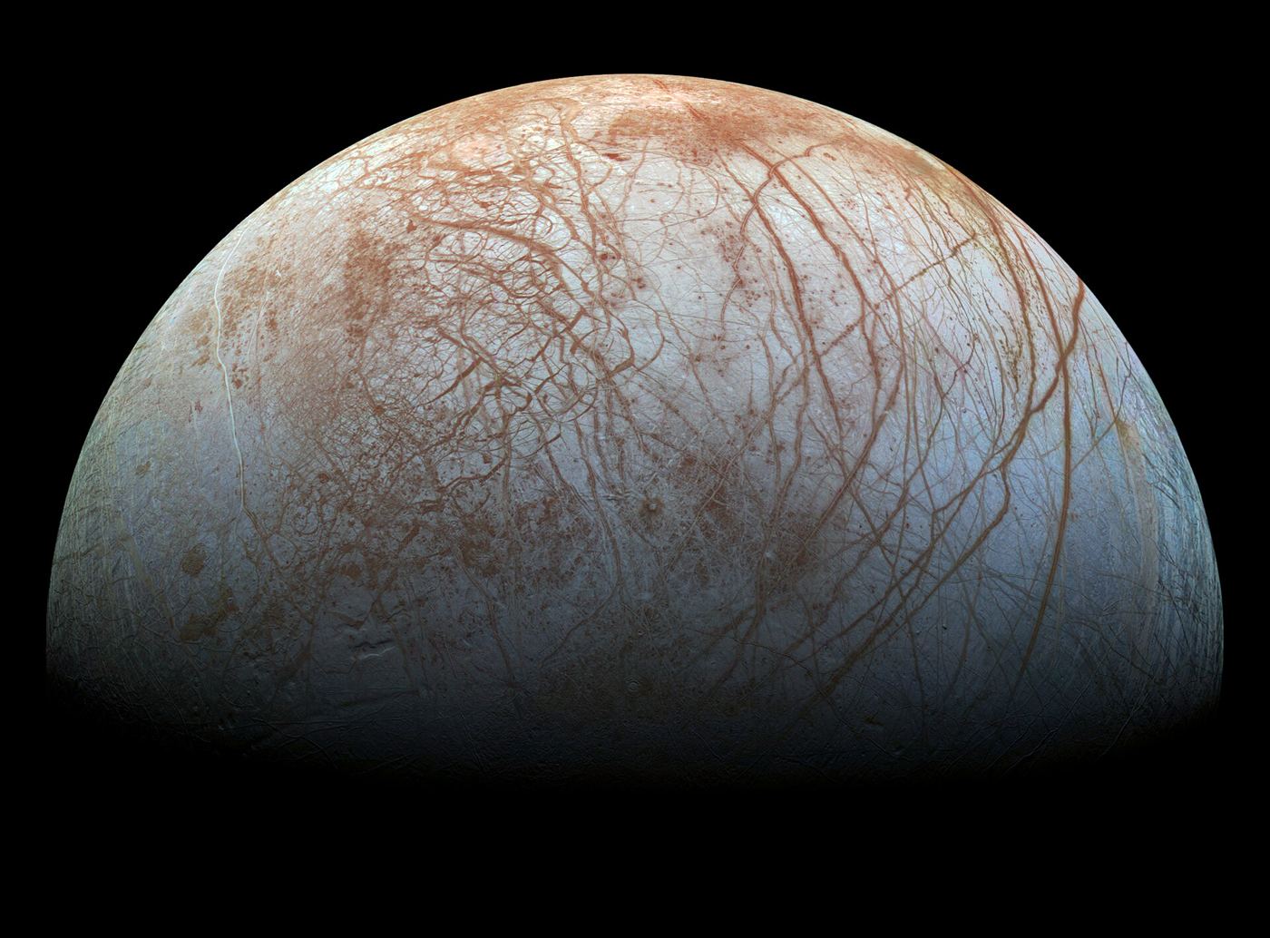 Jupiter's icy moon Europa seen from space, its cracked white and brown ice shell glowing against black space.